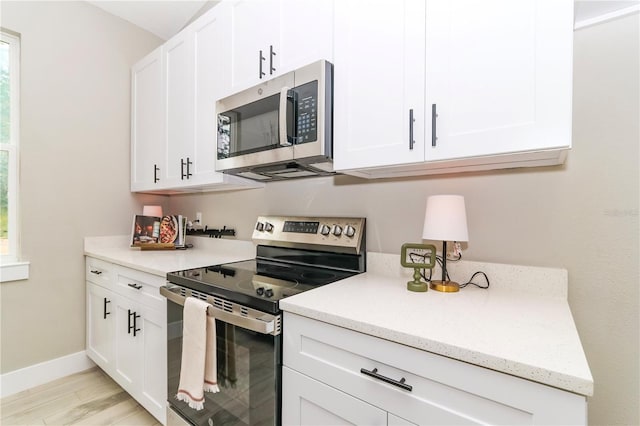 kitchen with appliances with stainless steel finishes, light wood-type flooring, white cabinetry, and light stone counters