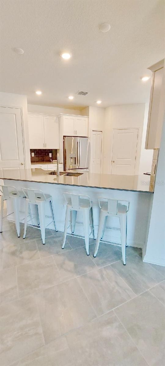 kitchen with kitchen peninsula, stainless steel fridge, white cabinetry, and a kitchen breakfast bar