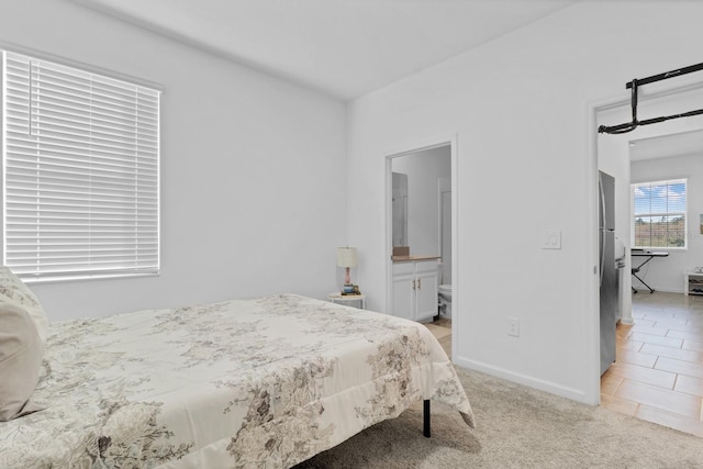 carpeted bedroom with stainless steel refrigerator and ensuite bath