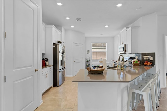 kitchen featuring a kitchen bar, sink, white cabinetry, tasteful backsplash, and stainless steel appliances