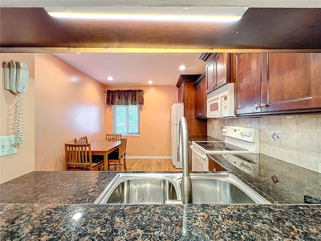 kitchen with hardwood / wood-style floors, white appliances, dark stone countertops, and backsplash