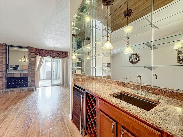 bar featuring pendant lighting, sink, beverage cooler, and light hardwood / wood-style flooring