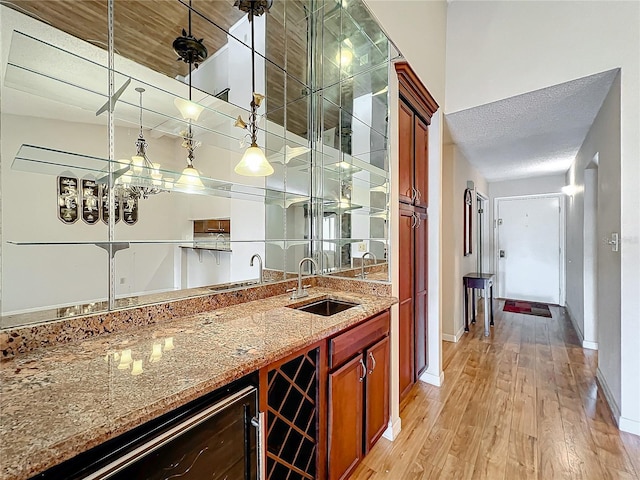 bar with sink, hanging light fixtures, beverage cooler, light stone counters, and light hardwood / wood-style flooring