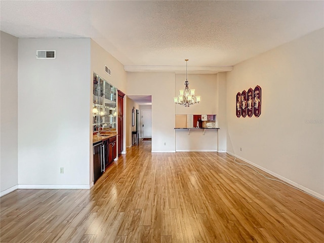 unfurnished living room with sink, an inviting chandelier, a textured ceiling, and light wood-type flooring