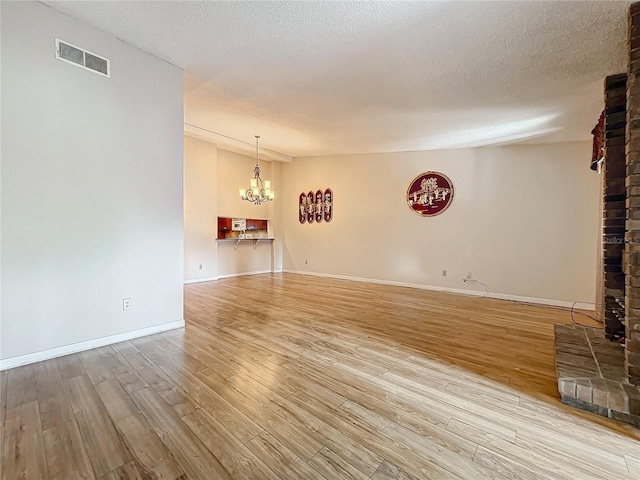 unfurnished living room with a textured ceiling, a brick fireplace, a notable chandelier, and light wood-type flooring