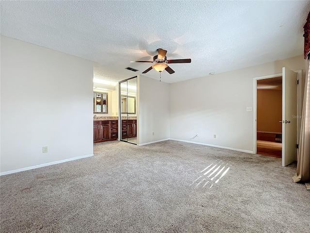 unfurnished bedroom with ensuite bathroom, ceiling fan, light colored carpet, and a textured ceiling