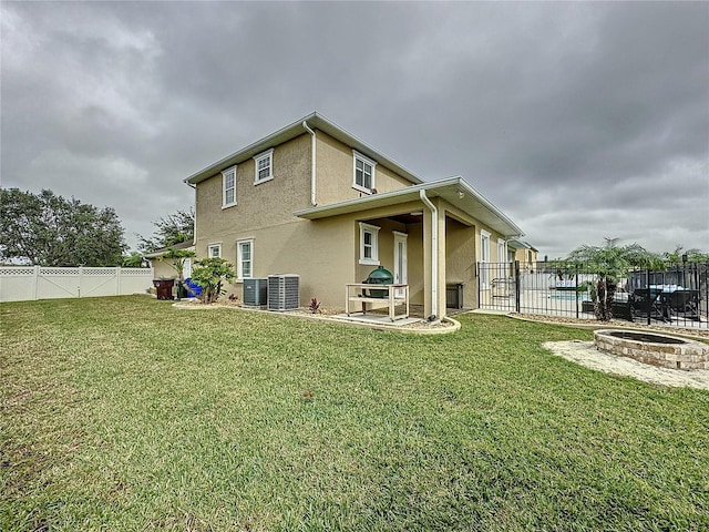 back of house featuring a lawn, central AC unit, and an outdoor fire pit