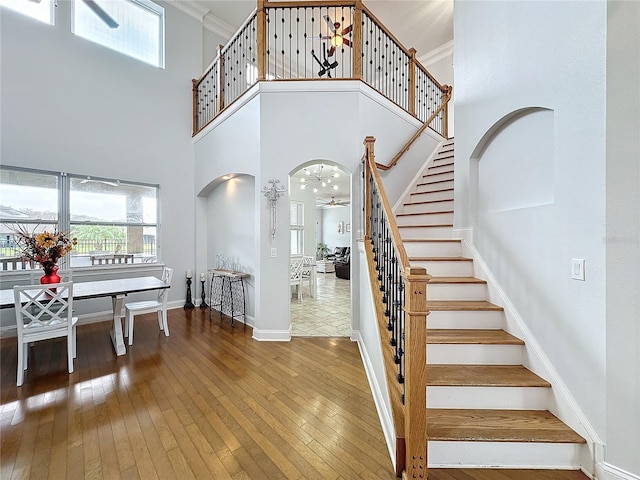 stairs with hardwood / wood-style floors, ceiling fan, a towering ceiling, and ornamental molding