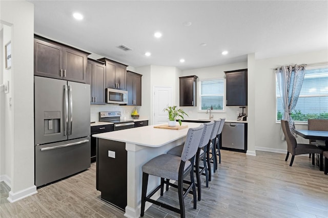 kitchen with a kitchen bar, appliances with stainless steel finishes, dark brown cabinets, light hardwood / wood-style floors, and a kitchen island