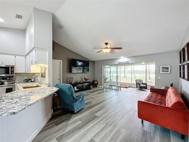 living room with ceiling fan, sink, light wood-type flooring, a textured ceiling, and lofted ceiling