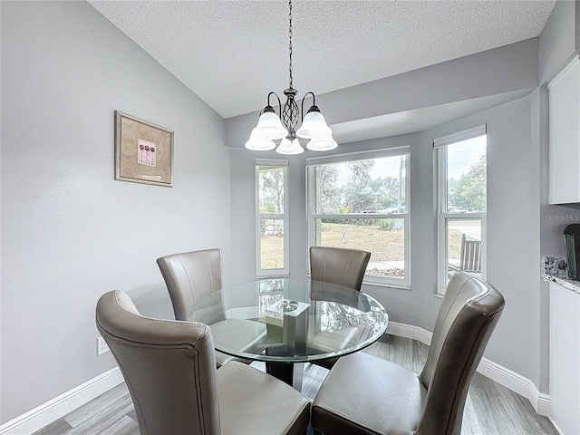 dining space with a textured ceiling, a chandelier, light hardwood / wood-style flooring, and vaulted ceiling