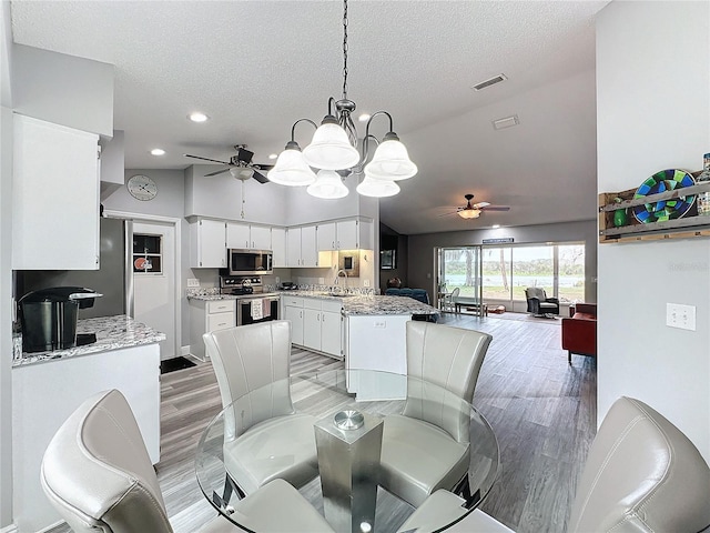 dining area featuring ceiling fan, vaulted ceiling, a textured ceiling, and wood-type flooring