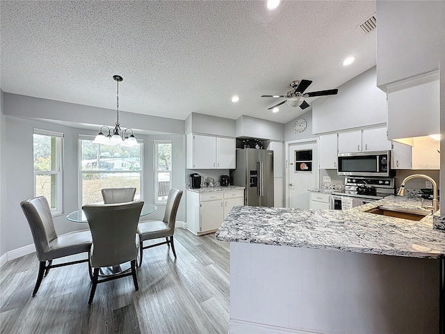 kitchen featuring white cabinets, stainless steel appliances, vaulted ceiling, and decorative light fixtures