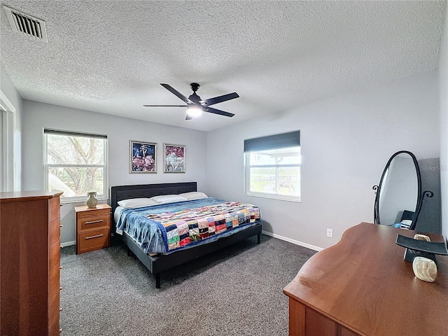 bedroom with ceiling fan, multiple windows, a textured ceiling, and dark colored carpet