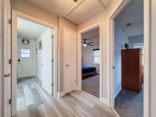 hallway with light colored carpet and a textured ceiling