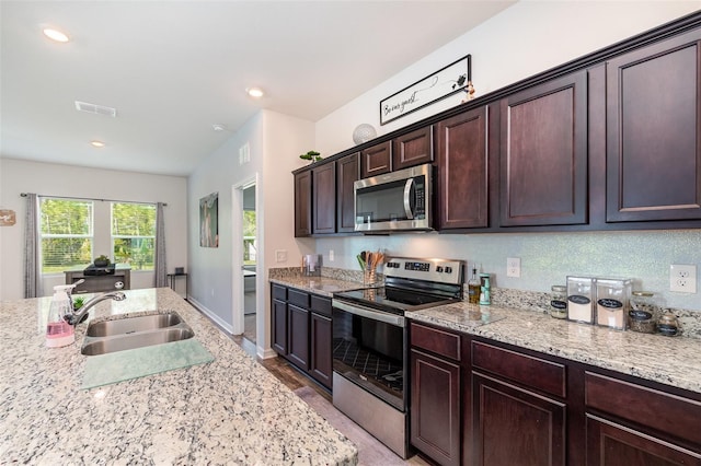 kitchen with light stone counters, sink, stainless steel appliances, and dark brown cabinets