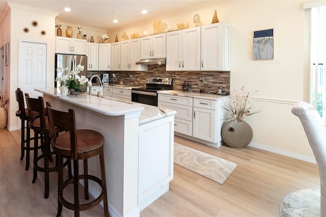 kitchen with a kitchen bar, light stone counters, stainless steel appliances, white cabinetry, and an island with sink