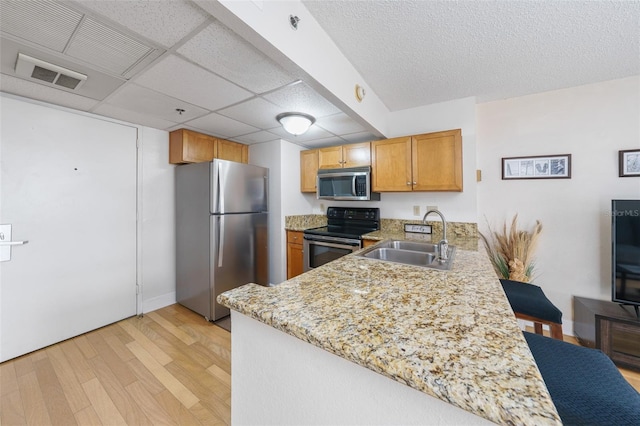 kitchen with light stone countertops, appliances with stainless steel finishes, kitchen peninsula, sink, and light hardwood / wood-style floors