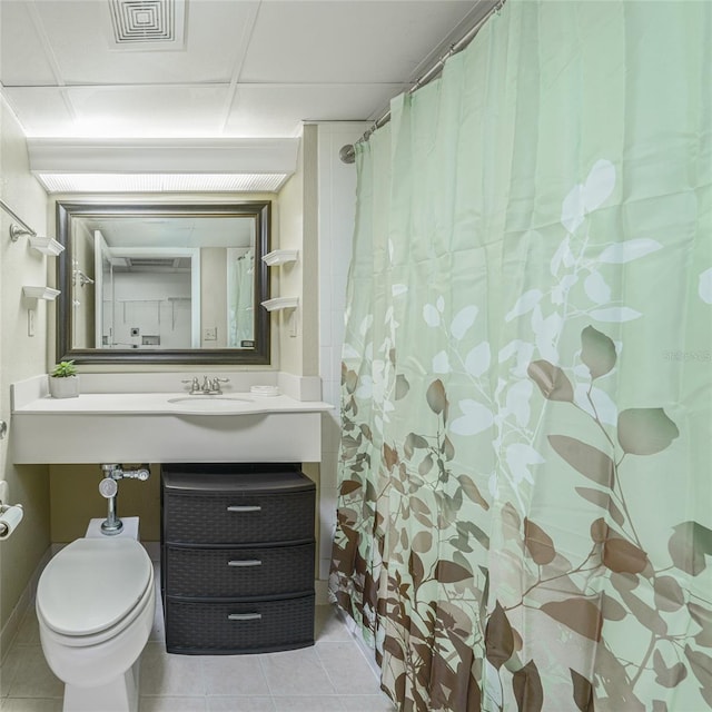 bathroom with tile patterned floors, a paneled ceiling, sink, and toilet