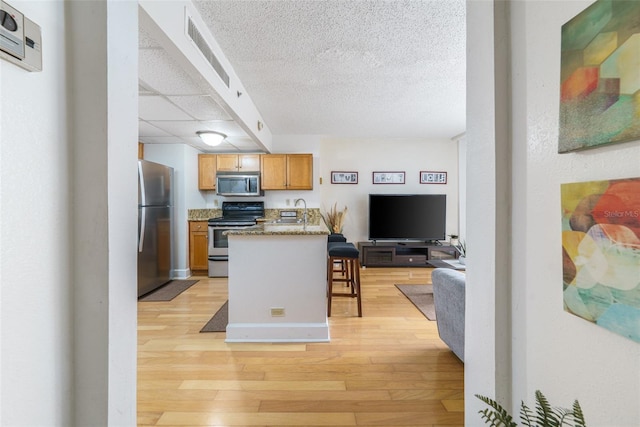 kitchen with light stone counters, a textured ceiling, stainless steel appliances, light hardwood / wood-style flooring, and a breakfast bar area