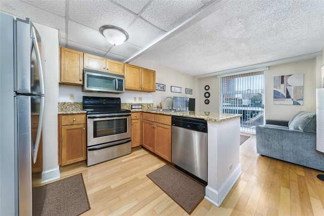 kitchen with a drop ceiling, sink, appliances with stainless steel finishes, light hardwood / wood-style floors, and kitchen peninsula