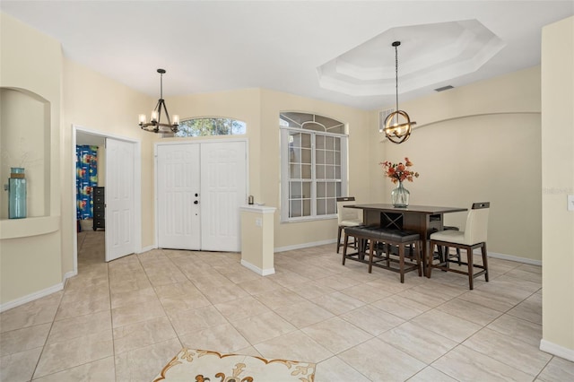 foyer with a tray ceiling, light tile patterned floors, and a notable chandelier