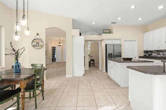 kitchen with backsplash, hanging light fixtures, stainless steel fridge, light tile patterned floors, and white cabinetry