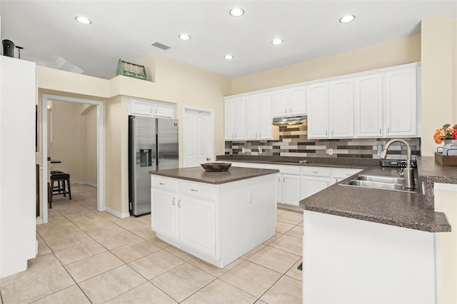 kitchen with sink, stainless steel refrigerator with ice dispenser, light tile patterned floors, a kitchen island, and white cabinetry