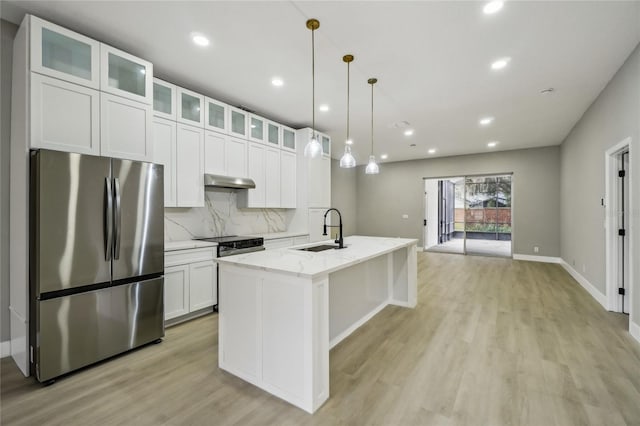 kitchen featuring sink, light stone counters, stainless steel fridge, a center island with sink, and white cabinets