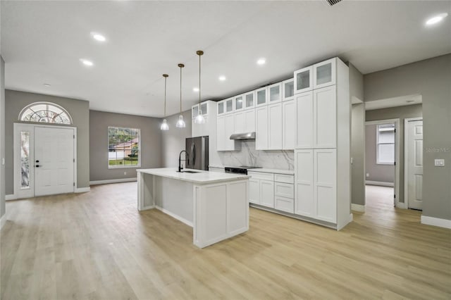 kitchen with stainless steel refrigerator, white cabinetry, tasteful backsplash, pendant lighting, and a kitchen island with sink