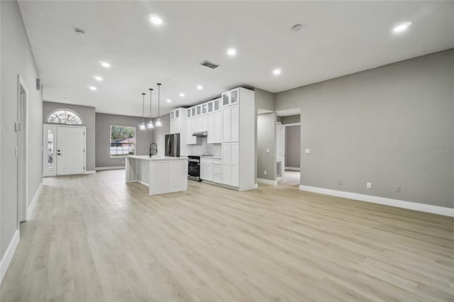 kitchen with a center island with sink, white cabinets, hanging light fixtures, appliances with stainless steel finishes, and light hardwood / wood-style floors