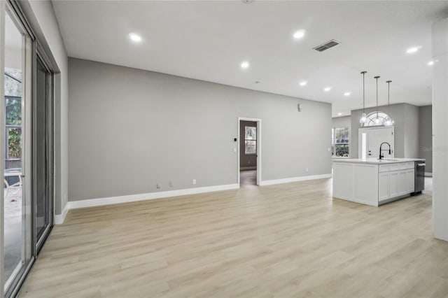 kitchen with sink, hanging light fixtures, light hardwood / wood-style flooring, a kitchen island with sink, and white cabinets