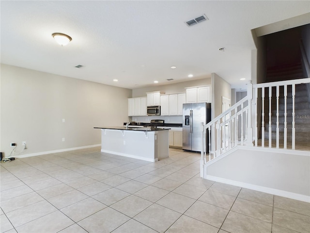 kitchen featuring white cabinetry, an island with sink, a kitchen bar, light tile patterned flooring, and appliances with stainless steel finishes