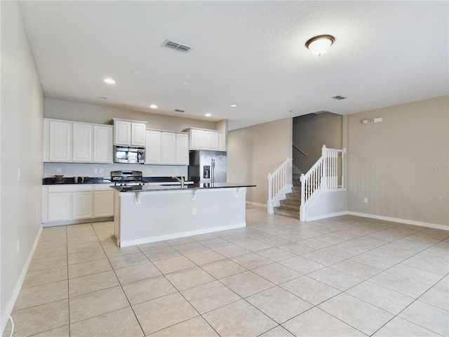 kitchen with sink, light tile patterned floors, an island with sink, appliances with stainless steel finishes, and white cabinetry