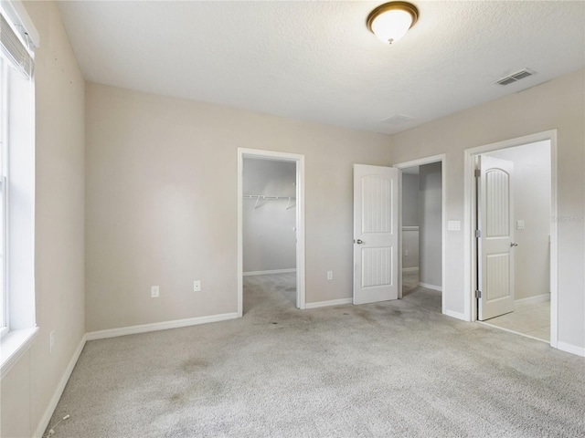 unfurnished bedroom with a walk in closet, a closet, light colored carpet, and multiple windows