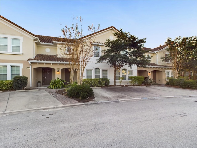 view of front of property featuring stucco siding, a tile roof, and uncovered parking