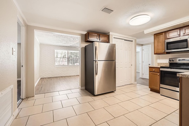 kitchen with light tile patterned flooring, a textured ceiling, stainless steel appliances, and brick wall