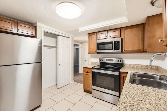 kitchen featuring light stone counters, a textured ceiling, stainless steel appliances, sink, and light tile patterned floors