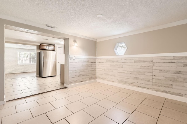 interior space with stainless steel fridge, wooden walls, light tile patterned floors, and a textured ceiling