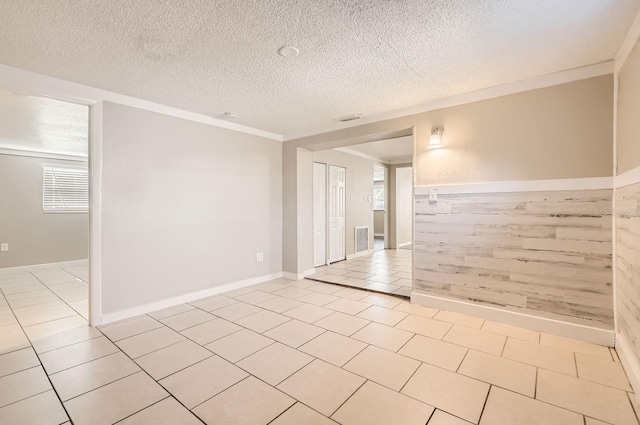 empty room featuring light tile patterned flooring, ornamental molding, and a textured ceiling