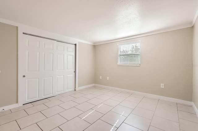 unfurnished bedroom featuring light tile patterned flooring, ornamental molding, and a closet