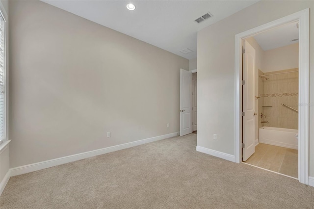 unfurnished bedroom featuring light carpet, a walk in closet, ensuite bathroom, and a closet