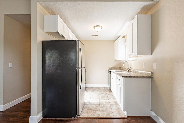 kitchen with appliances with stainless steel finishes, a textured ceiling, light stone counters, sink, and white cabinetry