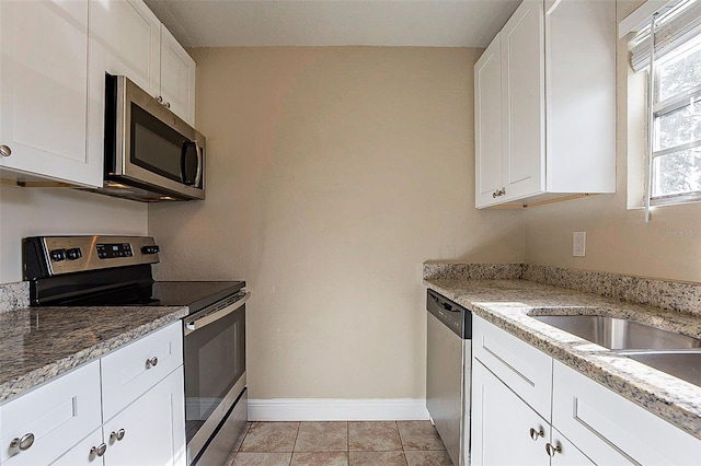 kitchen with stainless steel appliances, light tile patterned flooring, light stone countertops, and white cabinets