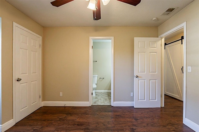 unfurnished bedroom with dark hardwood / wood-style floors, a closet, connected bathroom, a barn door, and ceiling fan