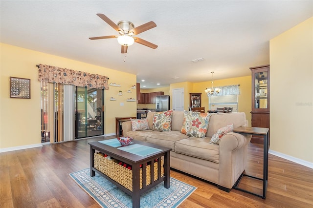 living room with ceiling fan with notable chandelier and light wood-type flooring