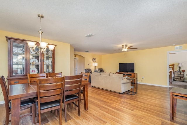 dining room featuring ceiling fan with notable chandelier, a textured ceiling, and light wood-type flooring