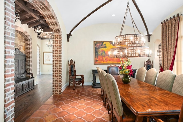 dining space with lofted ceiling, a fireplace, a notable chandelier, wood-type flooring, and brick ceiling