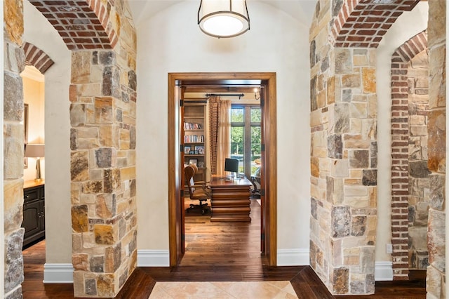 corridor with dark hardwood / wood-style floors, vaulted ceiling, and brick ceiling