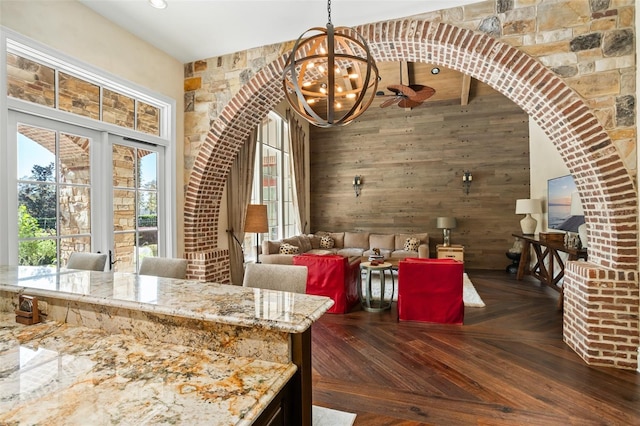 dining area with wood walls, dark parquet floors, and ceiling fan with notable chandelier